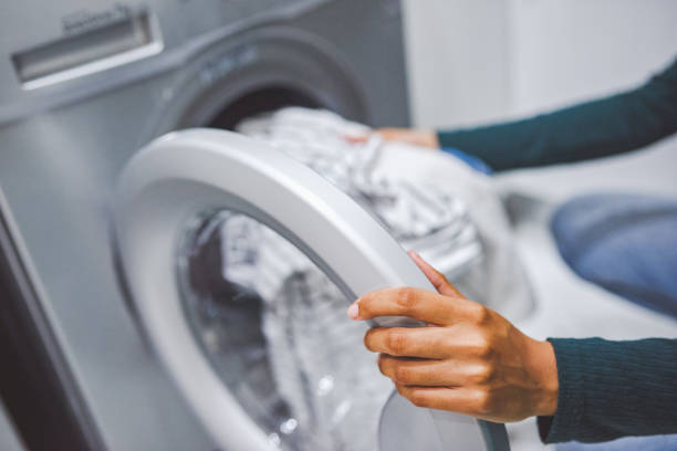 A person is loading striped laundry into the drum of a front-loading washing machine.