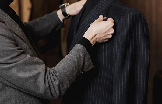 A person adjusts the collar of a dark pinstripe suit jacket on a mannequin.