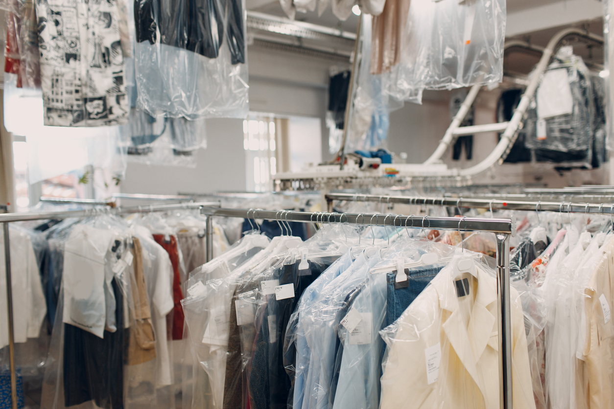 Racks of clothing covered in plastic hangers inside a dry cleaning facility, with garments organized and ready for pickup.