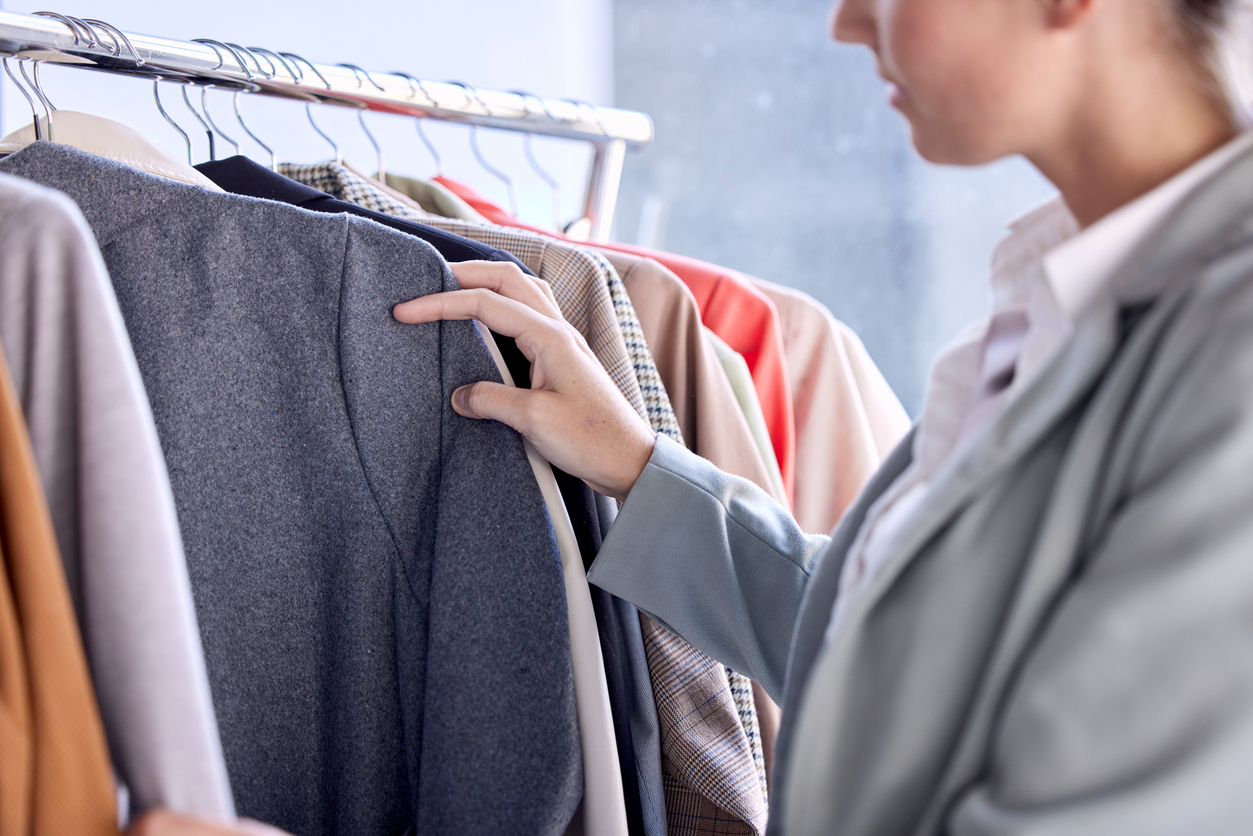 Person browsing and touching clothing items hanging on a rack, including jackets and coats in various colors and patterns.
