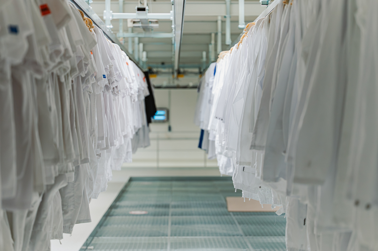Rows of white lab coats hang on racks in a bright, modern facility with a grated metal floor.
